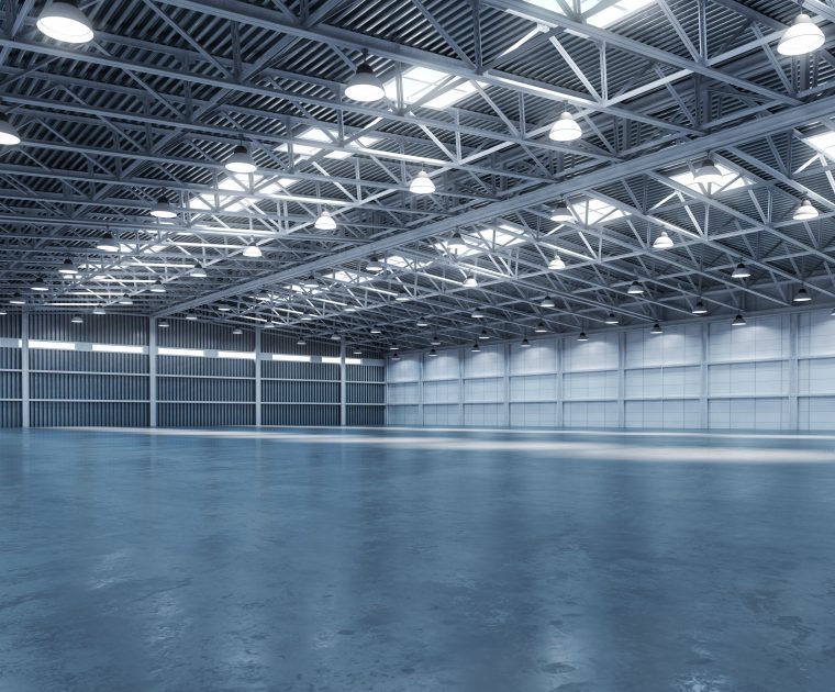 An empty, spacious industrial warehouse with high ceilings and bright lighting.