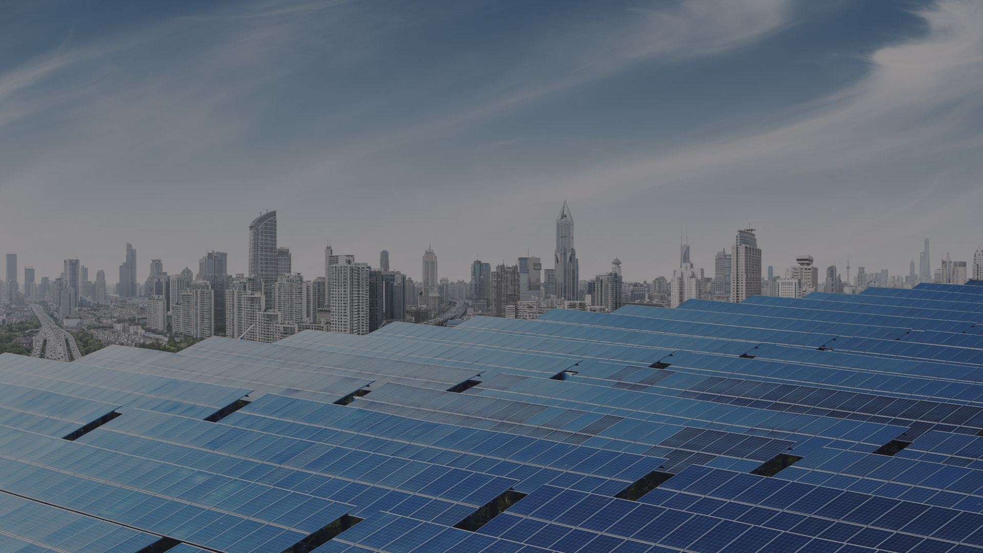 Solar panels in front of a city skyline under a cloudy sky.