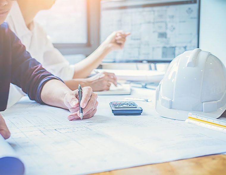 Architects discussing blueprints and calculations at a worktable.