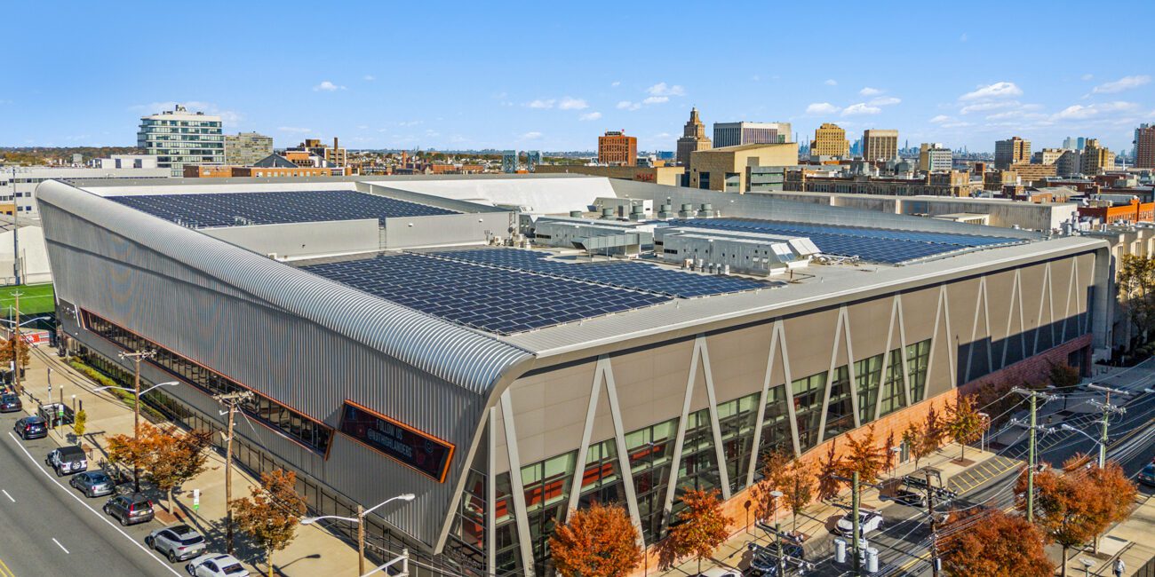 A large building with solar panels on the roof and a city skyline in the background.