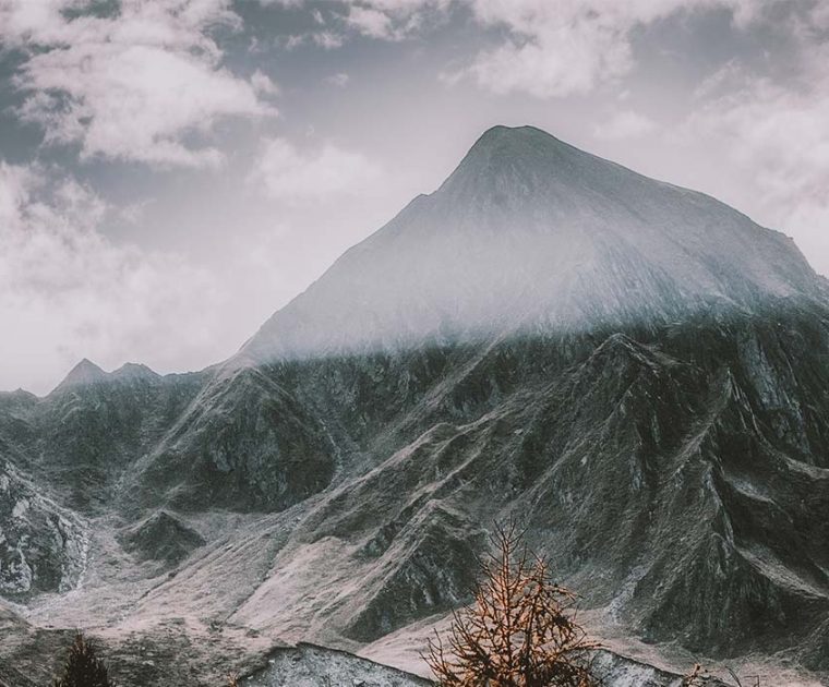 Misty mountain peak with rugged terrain under a cloudy sky.
